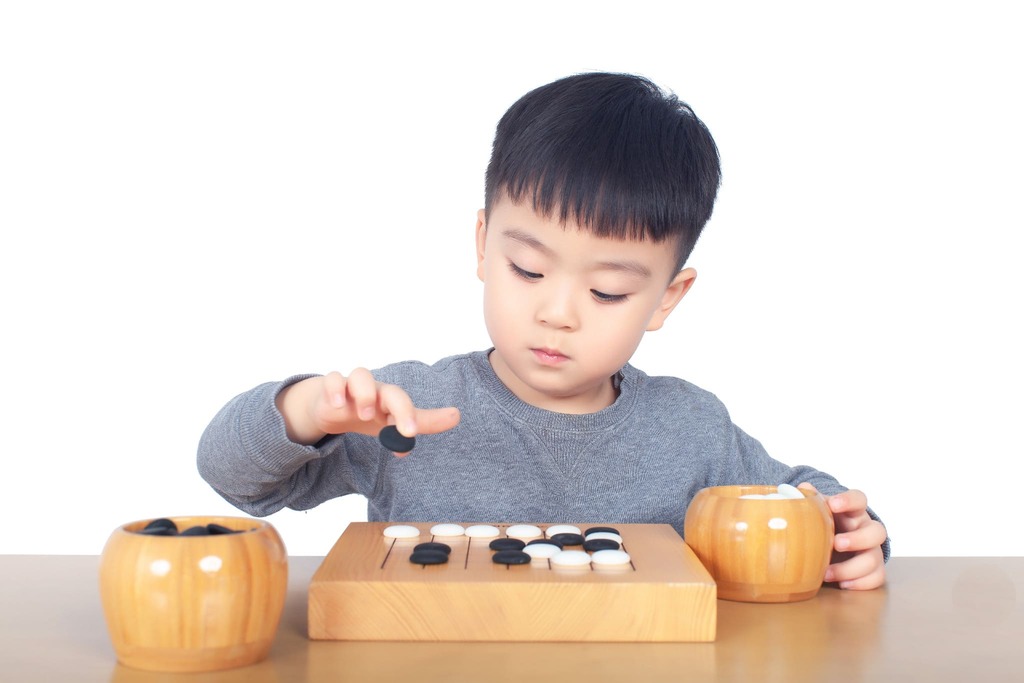 A young child concentrating while placing a black stone on a small Go board, beginning to explore the basics of Baduk