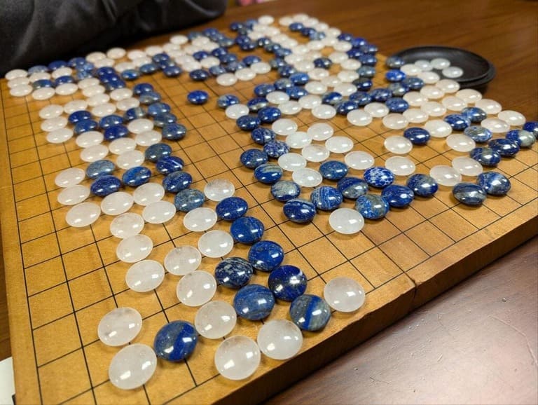 A close-up of a Go board featuring polished blue and white stones in the middle of a game.