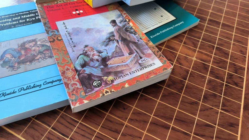 A close-up of Go books including titles from Yutopian and Kiseido on a wooden Go board.
