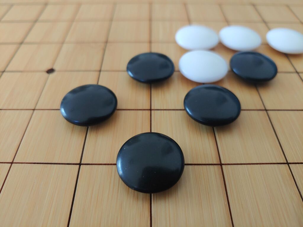 Close-up of black and white Go stones arranged to illustrate shape on a wooden Go board.