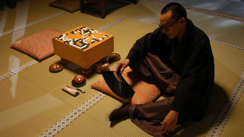 Man in traditional attire sitting near a Go board, reflecting on the match