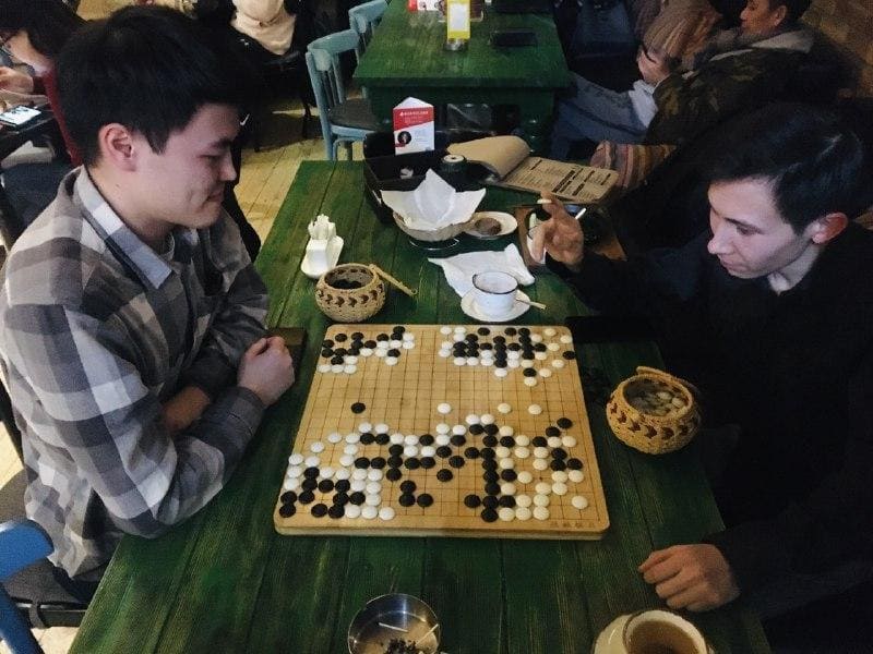 Two young men playing Go in a cozy Kyrgyz coffeehouse, enjoying a casual game over tea.