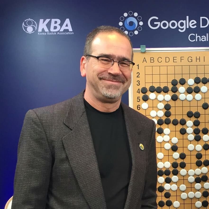 Chris Garlock smiling beside a demonstration Go board at the Google DeepMind Challenge Match.