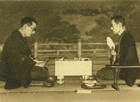Sepia-toned archival image of two men in kimono seated across a Go board during a formal match.