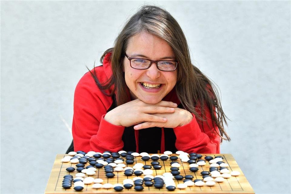 A smiling Go player leaning over a Go board filled with black and white stones.