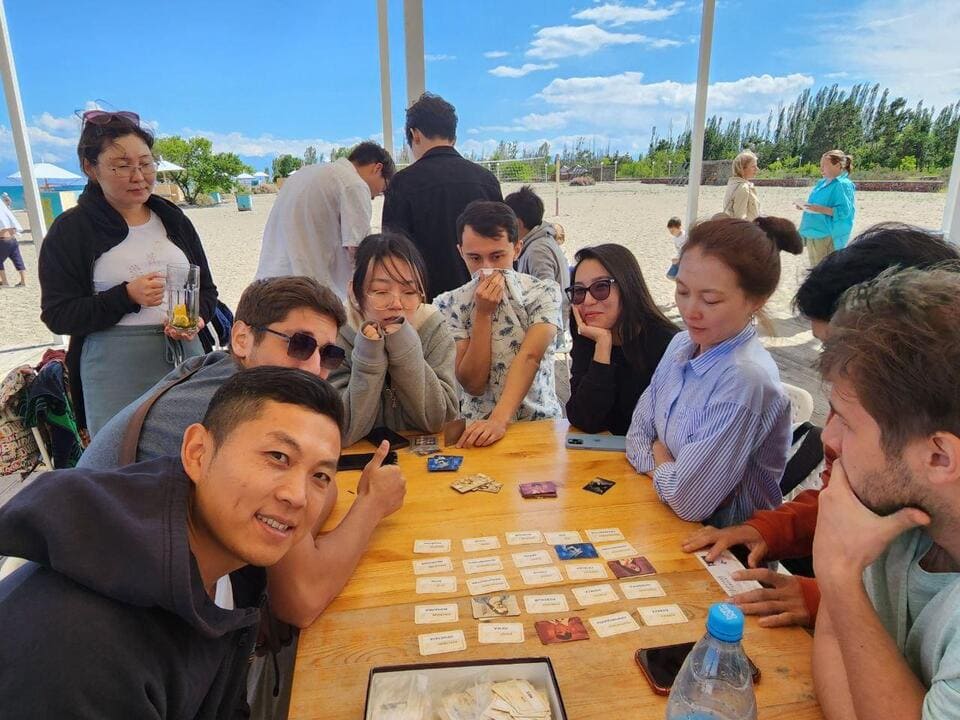 Festival participants sitting around a table and playing board games near the beach at Lake Issyk-Kul.