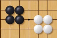 Close-up of a go board showing a 2x2 block of black stones and a 2x2 block of white stones facing each other.