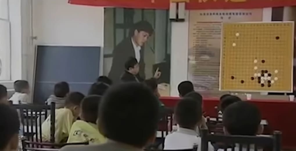 Teacher explaining Go strategy to students using a demonstration board