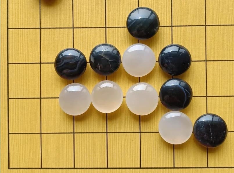 A close-up of polished agate (white) and onyx (black) Go stones arranged on a wooden Go board