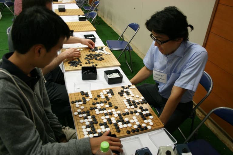 Two players facing each other over a full Go board during a tournament game at camp