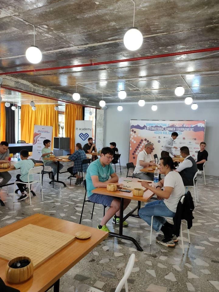 Participants playing Go inside a hall decorated with bright curtains and concrete ceiling.