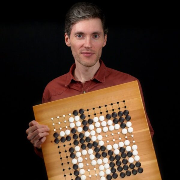 A man in a red shirt holding a Go board with a completed game position, posing for the camera.