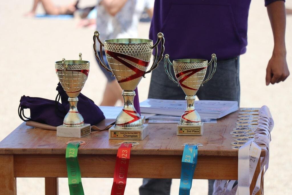 Three gold trophies and multiple medals displayed on a wooden table at the beach.