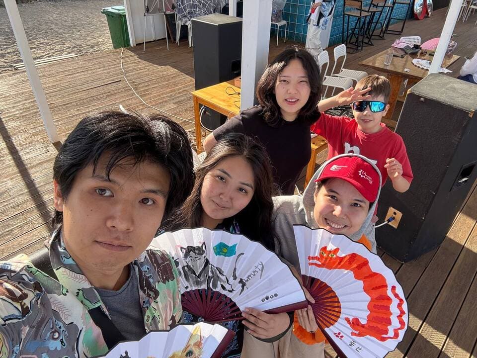 A group of Issyk-Kul Cup participants taking a selfie while holding decorated paper fans.