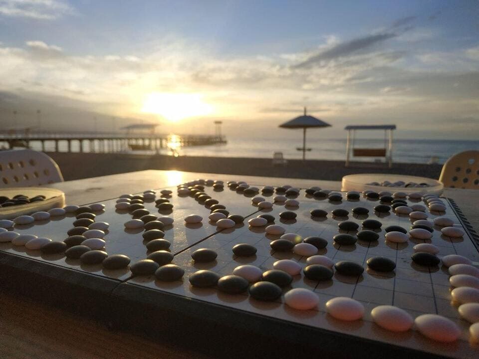 Go board with black and white stones at sunset by the beach and a long pier.