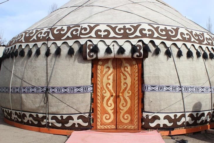 Decorated traditional Kyrgyz yurt with patterned fabric and wooden doors.