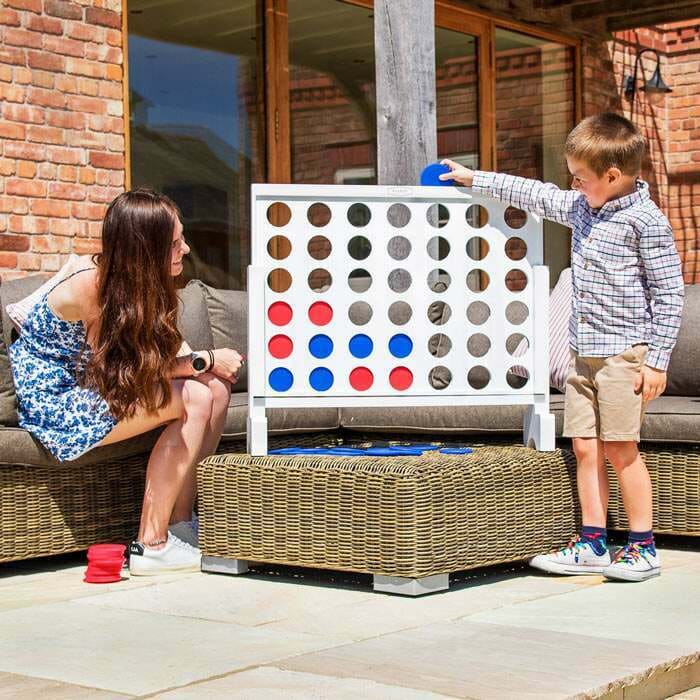 A woman and a young boy play a large outdoor Connect Four game on a patio.
