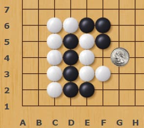 Go board corner diagram showing a tight black-and-white stone formation with a coin placed beside the position for scale.