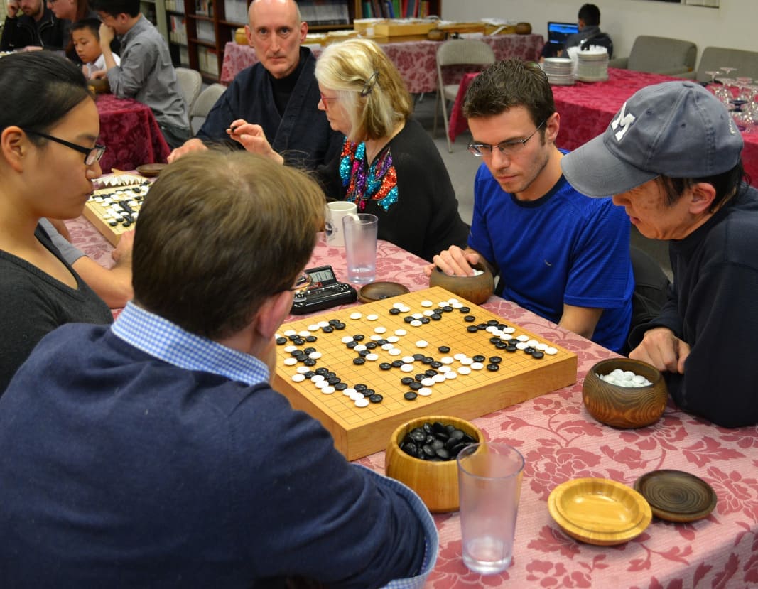 Group of players gathered around a Go board during a casual club game