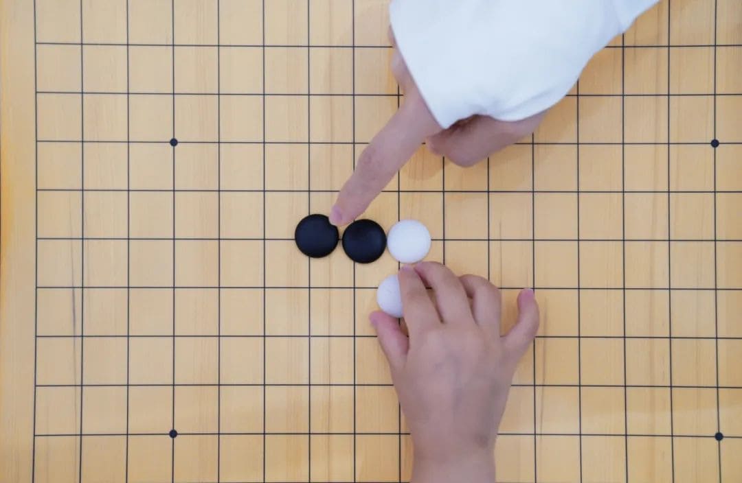 A teacher pointing at stones on a Go board while helping a child understand capture and connection