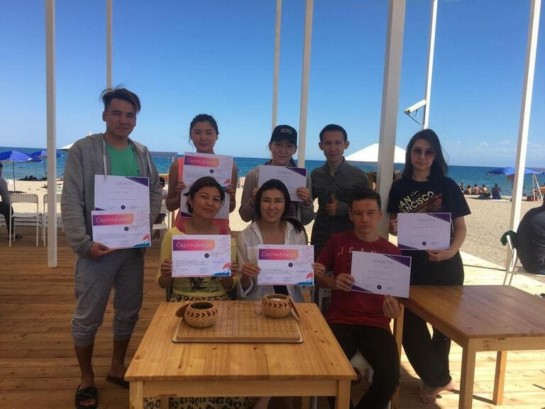A group of Go participants holding certificates near the beach at the Issyk-Kul Cup.