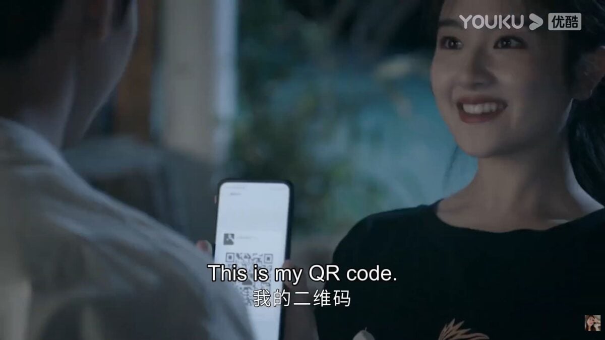A scene from GO Into Your Heart showing a woman holding up her phone and displaying a QR code.