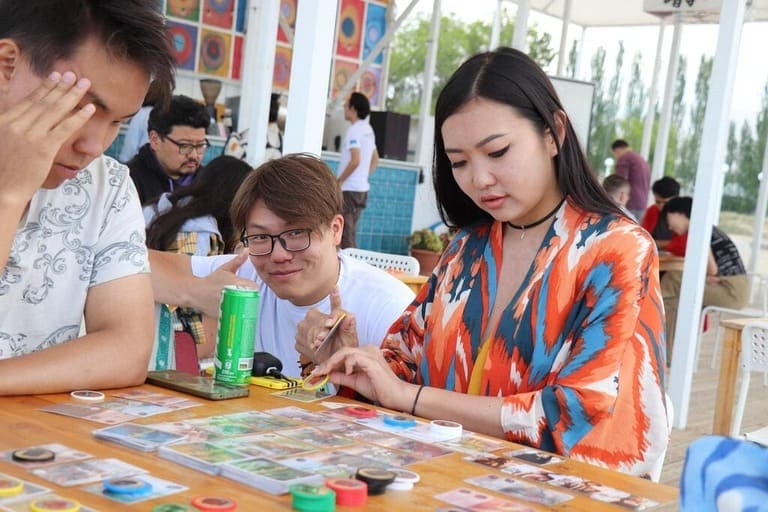 Participants playing a colorful card game at an outdoor festival by the beach.