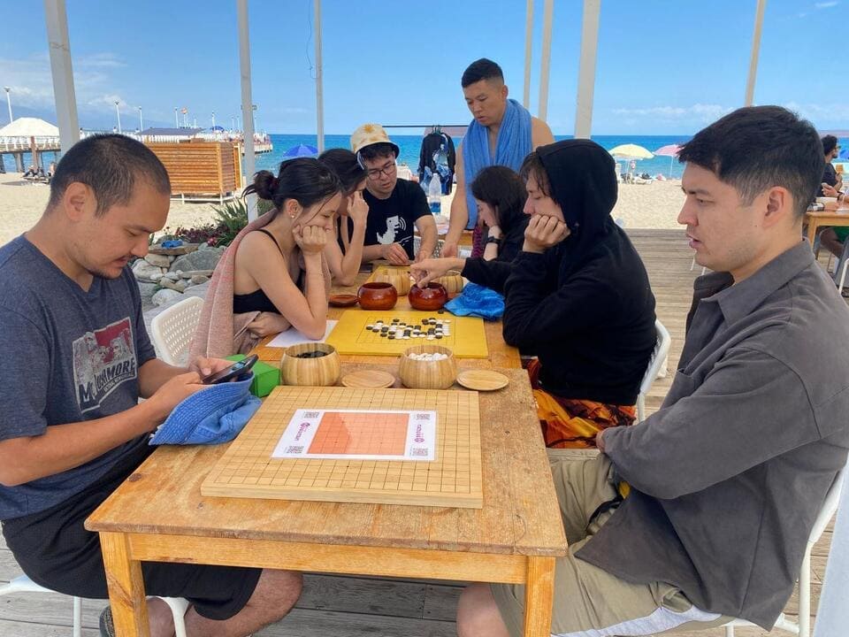 Players practicing Go under a canopy near the beach with colorful boards.