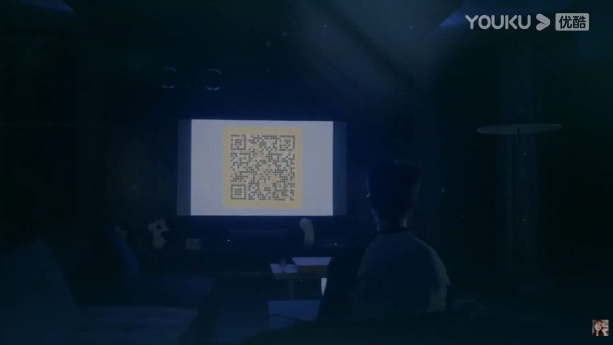 A dark interior scene from GO Into Your Heart showing a large screen with a completed QR code displayed in front of two viewers.