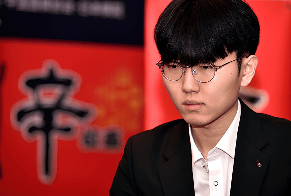 South Korean Go player Shin Jinseo in deep focus during the 25th Nongshim Cup, dressed in a dark suit against a red backdrop with Korean characters.