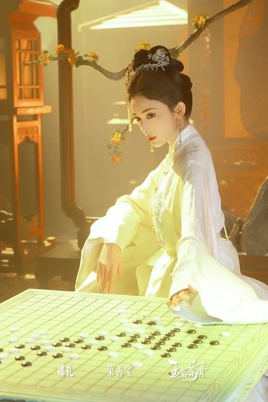 A stylized costume-drama still showing a woman in white seated beside a Go board with scattered black and white stones.