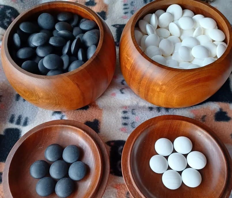 Wooden bowls filled with black and white Go stones, resting on a traditional Go board.