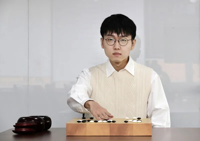 Professional Go player seated at a Go board, carefully analyzing a position during play