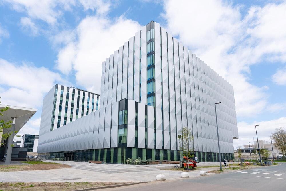 Exterior view of a modern white office building with a geometric facade under a bright cloudy sky.