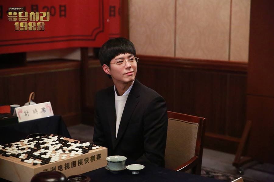 A still from Reply 1988 showing a young Go player seated at a tournament table beside a board filled with stones.