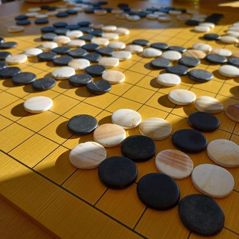 A smooth yellow Go board filled with shiny black and white stones mid-game.