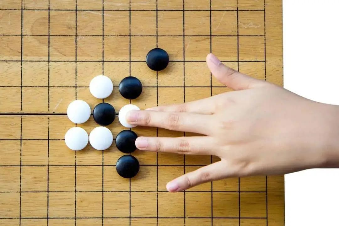 A player’s hand removing captured stones from a wooden Go board during a basic teaching exercise