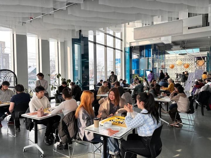 Young people playing Go and chatting in a stylish, light-filled Kyrgyz café.