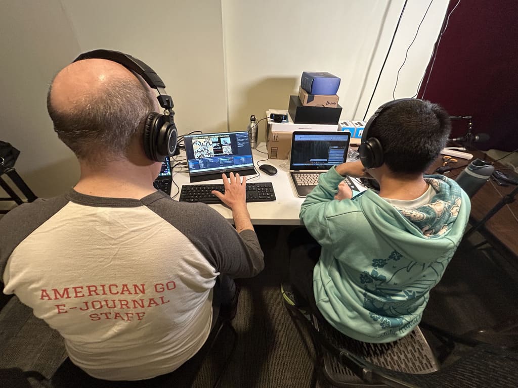 Two American Go E-Journal team members wearing headphones and operating laptops during a Go livestream.