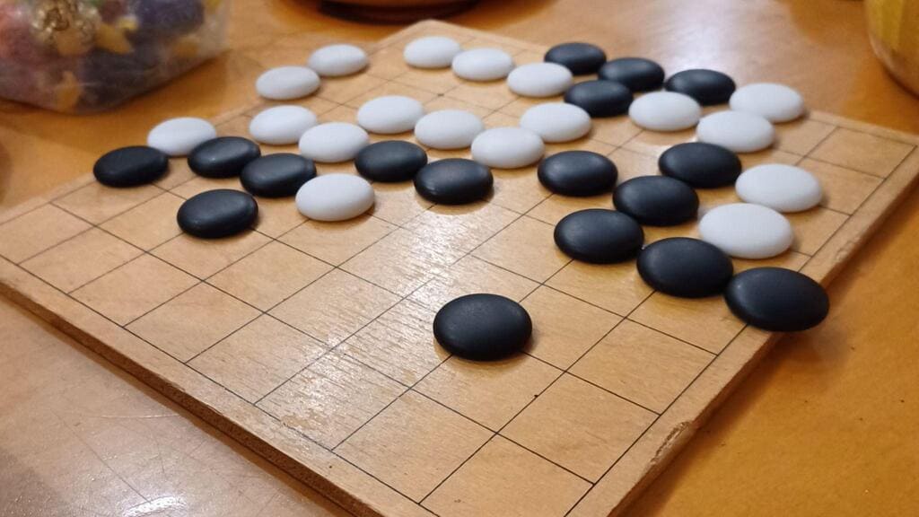 A side view of a 13x13 wooden Go board with black and white plastic stones placed in mid-game position on a table