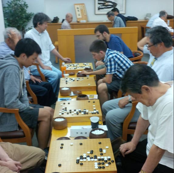 Several players sitting in rows and playing Go on wooden boards in a club room