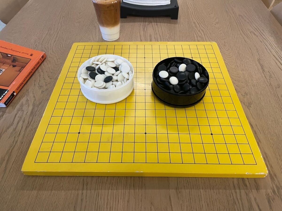 Yellow Go board with bowls of black and white stones on a wooden table