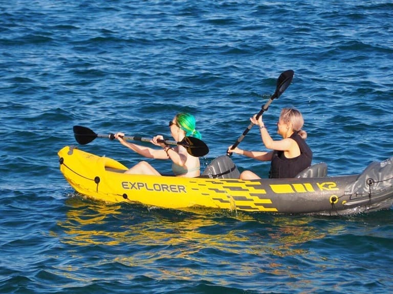 Two women kayaking on a blue lake in a yellow inflatable Explorer boat.