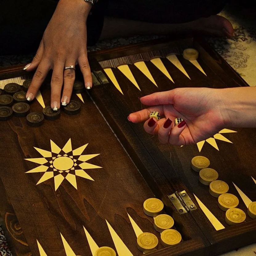 Close-up of hands playing backgammon, showing the board and pieces in action