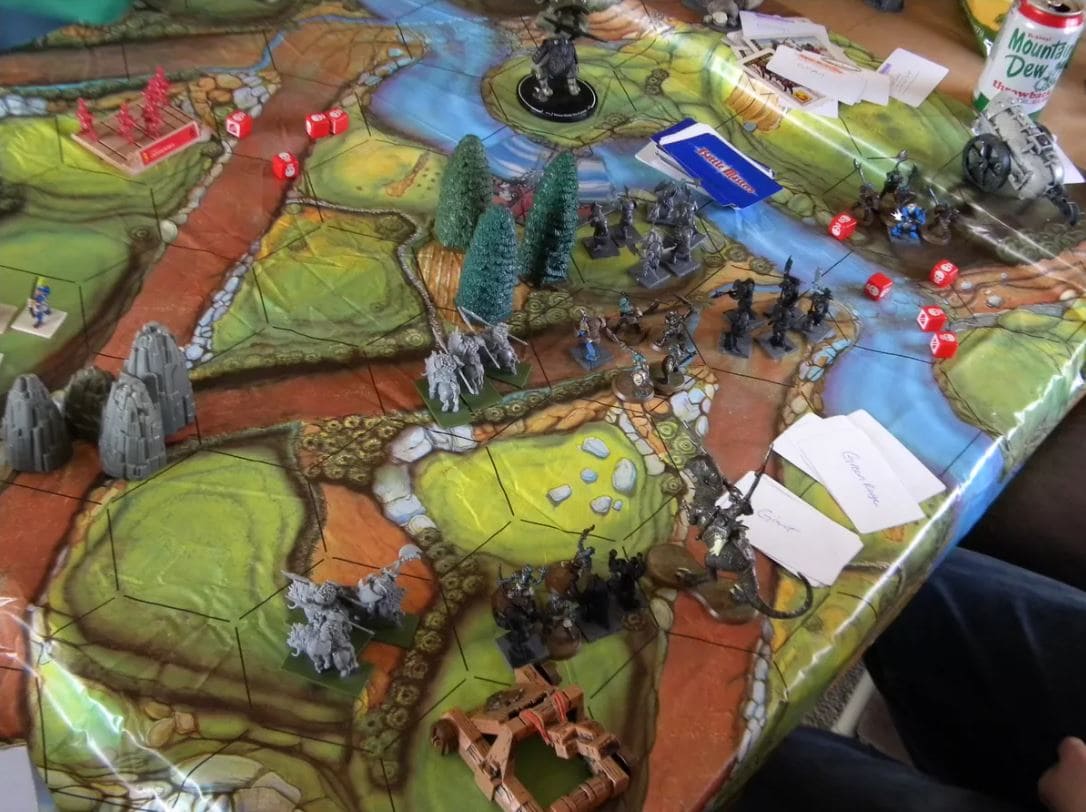 Battle Masters board game setup with figurines, dice, and terrain, depicting a battle between forces on a large hexagonal map.