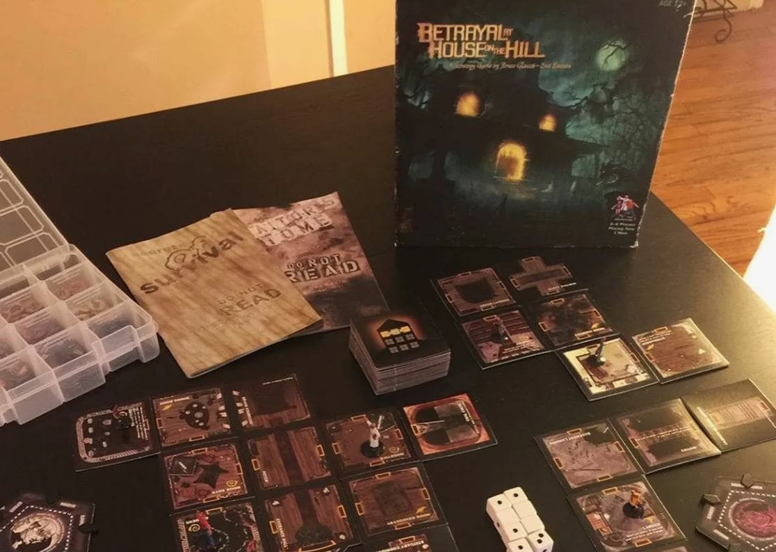 Components of the Betrayal at House on the Hill game, including miniature tiles and character sheets, set up for a spooky exploration.