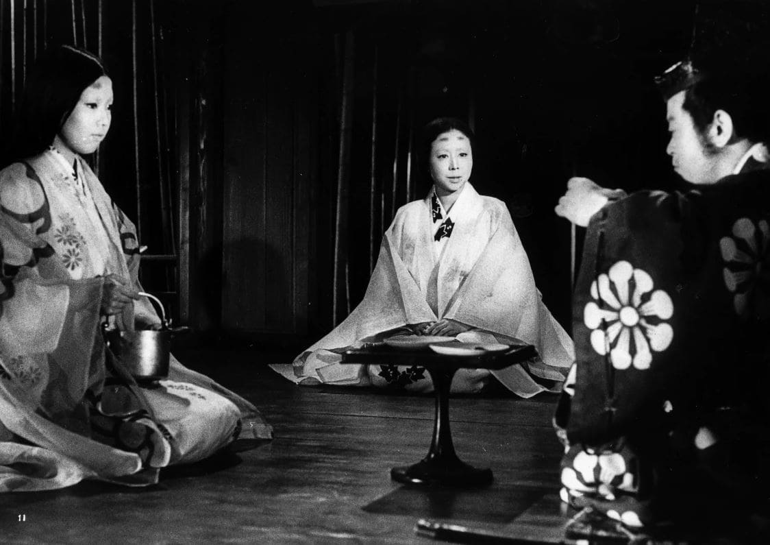 A black-and-white still from the film 'Black Cat in a Bamboo Grove' showing three characters performing a tea ceremony in traditional Japanese attire.