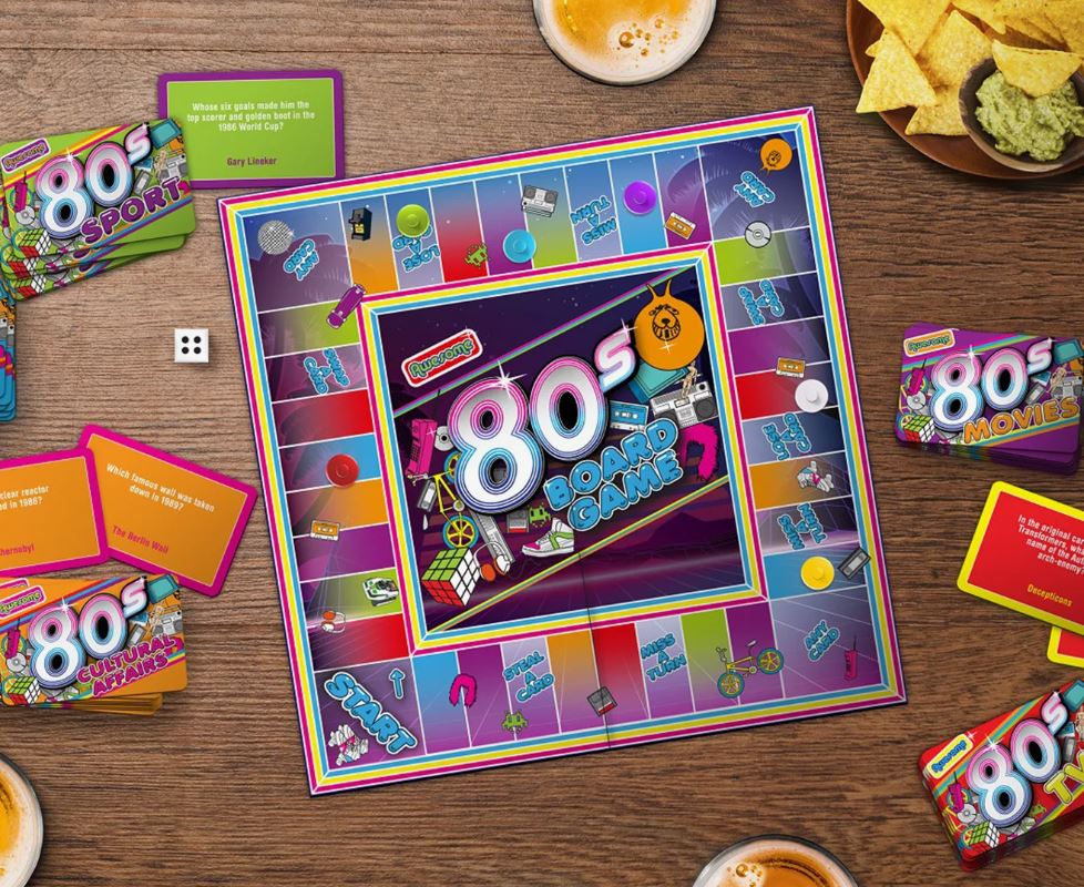 A colorful 80s-themed board game setup on a wooden table, featuring trivia cards about sports, movies, and culture, with dice, player pieces, and snacks like chips and guacamole nearby.