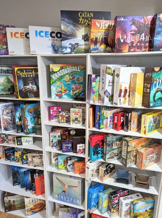 A variety of board games, including Catan and Splendor, displayed on shelves at a board game café.