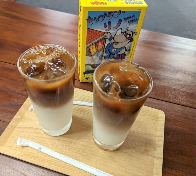 Two glasses of iced coffee next to a Captain Rhino board game at a board game café.